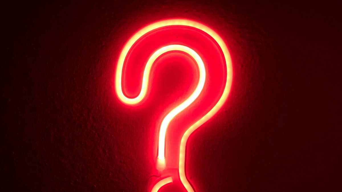 Un point d'interrogation lumineux rouge sur un mur sombre
