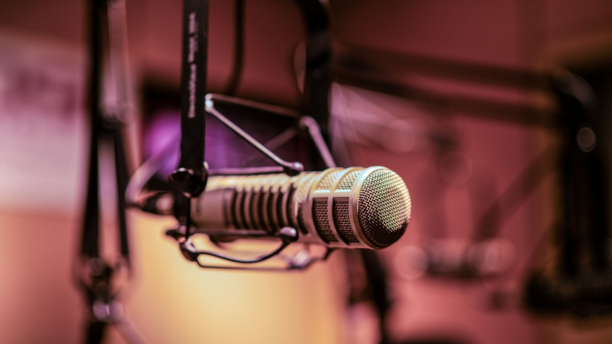 Un microphone de studio suspendu à un bras articulé devant un fond flou rosé