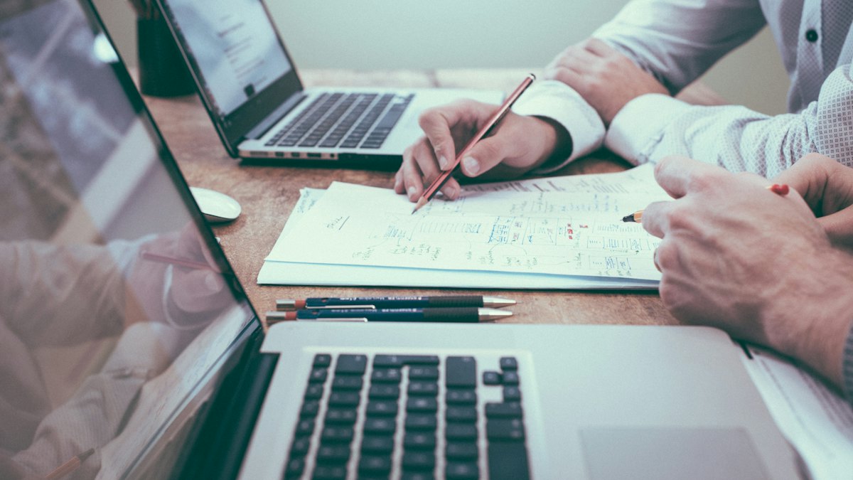 Deux personnes analysant des graphiques imprimés sur un bureau avec des ordinateurs portables